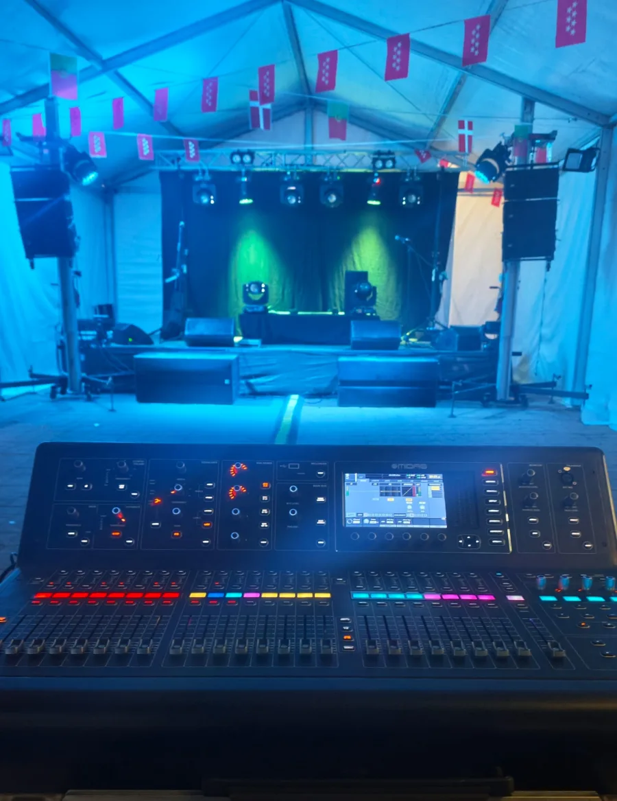 Mesa de mezclas digital frente a un escenario preparado con sistema de sonido e iluminación.